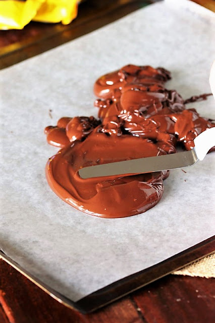 Spreading Melted Chocolate on Parchment Paper to Make Homemade Candy Image