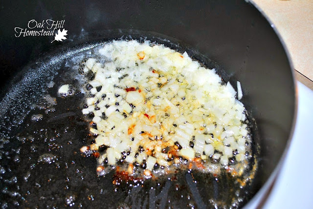 Chopped onions and minced garlic sauteing in butter in a black saucepan.