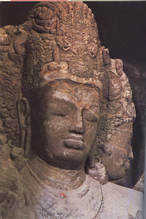 Shiva, the Great Lord. The central, outward looking aspect from the Mahesamurti carving in the rock temple at Elephanta. With its serene impassivity it represents the Absolute or Eternity. The masculine profile, symbolising his virility and will power, can be seen to the right. There is a third, out of view, which shows his feminine aspect. Early seventh century. 