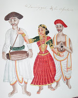 A watercolor illustration of a woman in colorful clothing and heavy jewelry, with a man in plainer clothing on either side. A handwritten caption reads "Dancing girl and her assistants."