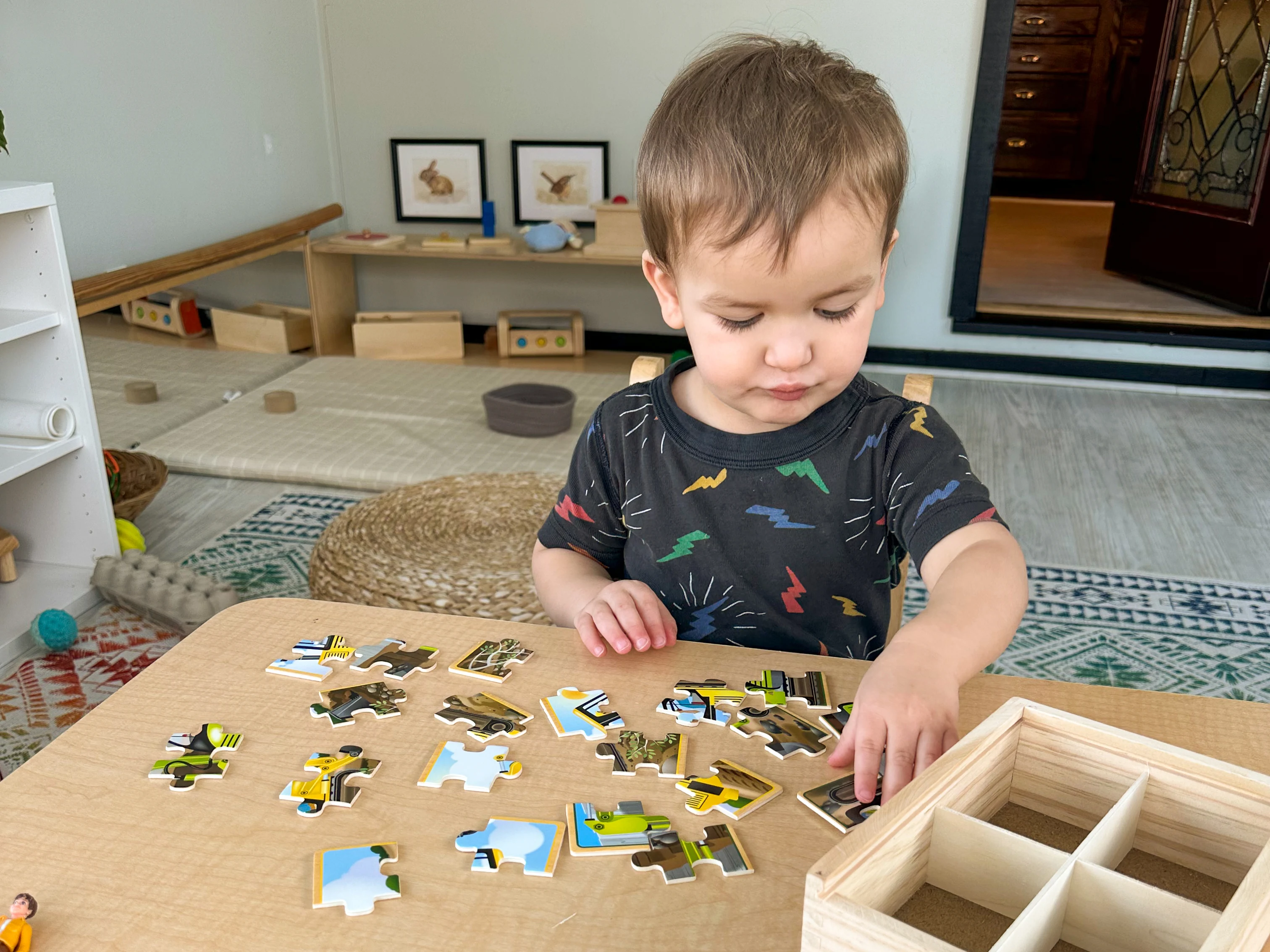 Montessori toddler sits at table to put together jigsaw puzzles.