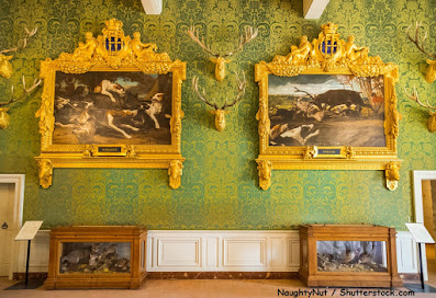  foto do salão do castelo de Chambord mostrando parede com papel verde e quadros de caças  