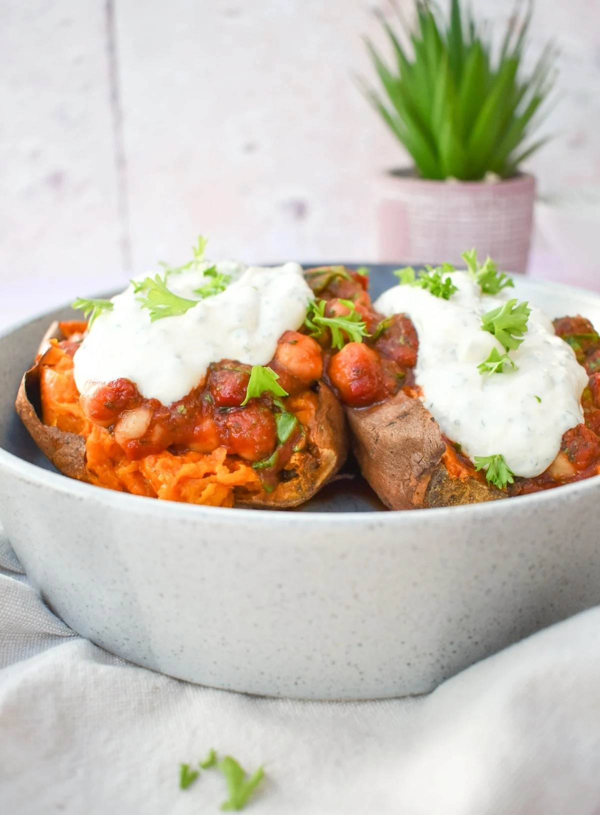 baked sweet potatoes in a bowl topped with chickpeas and a yoghurt topping