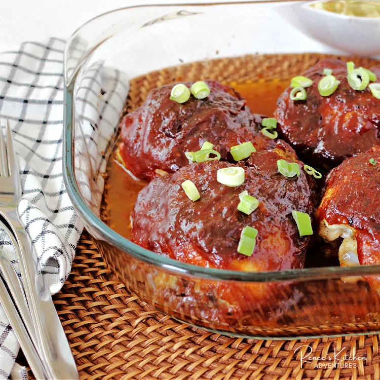 Sweet and Tangy Oven BBQ Chicken Thighs in a baking dish garnished with green onions with a towel next to it with forks on it.