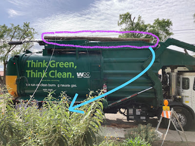 A large green recycling truck with a telephone pole resting on top.