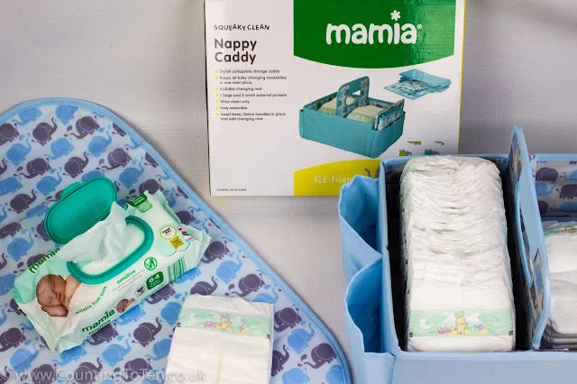 A blue nappy caddy with nappies in next to it's packaging and an opened changing mat with blue and grey elephant print