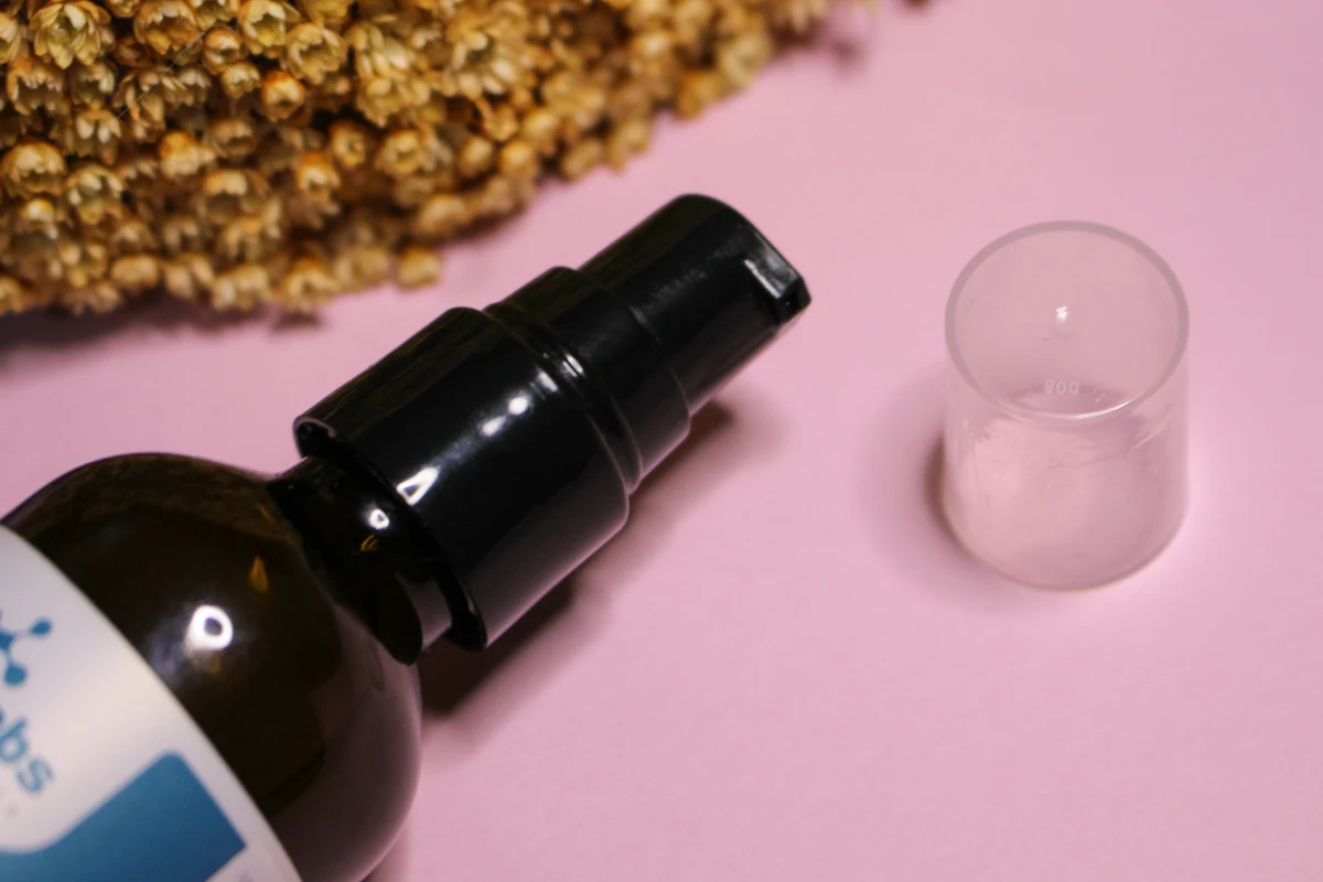 a glass bottle of the Qrxlabs 5% Niacinamide + Retinol Serum on a plain pink background