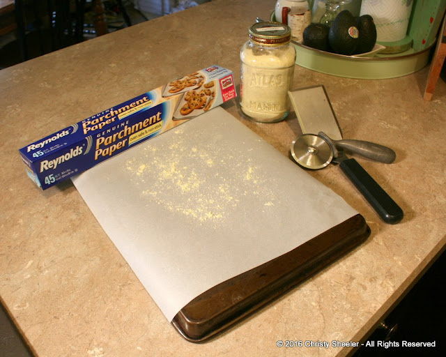 Baking sheet turned upside down, parchment paper cut to fit, and a sprinkle of cornmeal on the parchment paper.  Preparing to bake pizza in oven.