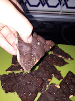 A hand holding chocolate bark in front of a pile of almond chocolate bark