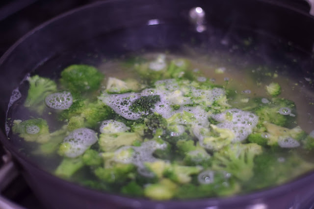 Broccoli steaming with the pasta in the pot on the stove.