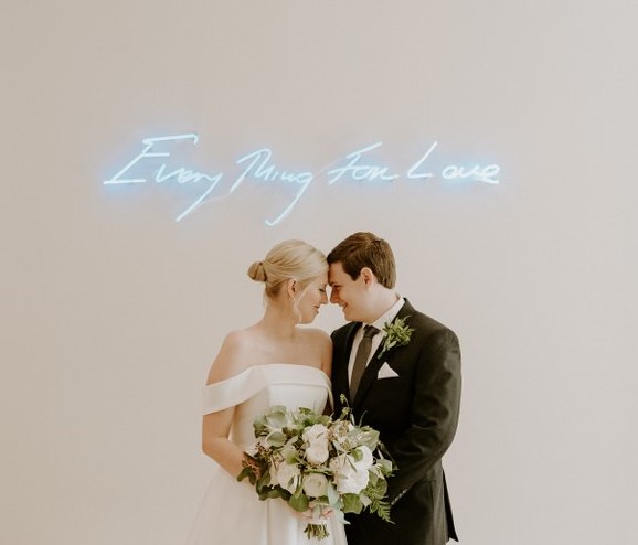 bride and groom in front of neon love sign