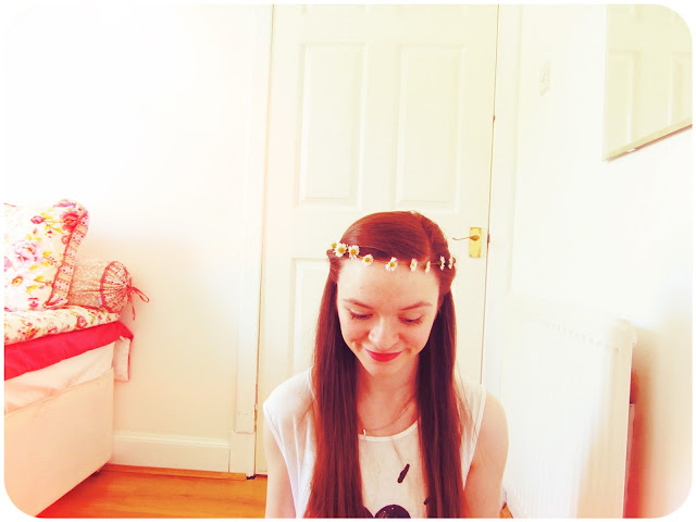 girl with long brown hair looks down smiling wearing daisy chain as hair band