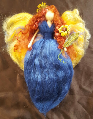 A hand made felted angel - she has long curly hair, a long blue gown, golden wings and carries sunflowers