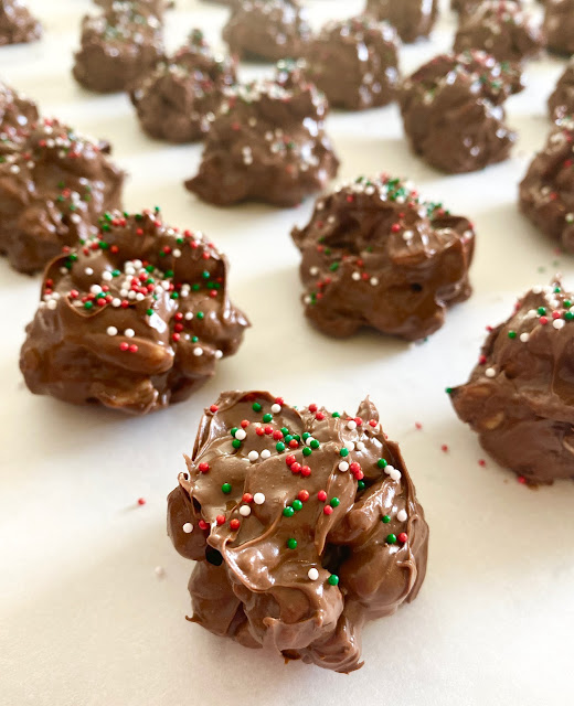 Close up of peanut clusters with sprinkles drying on parchment paper.