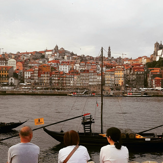 tês pessoas sentadas na margem do io Dour observando os barcos rabelos e a cidade do Porto