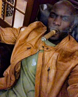 Bald African-American smoking a cigar wearing orange leather jacket