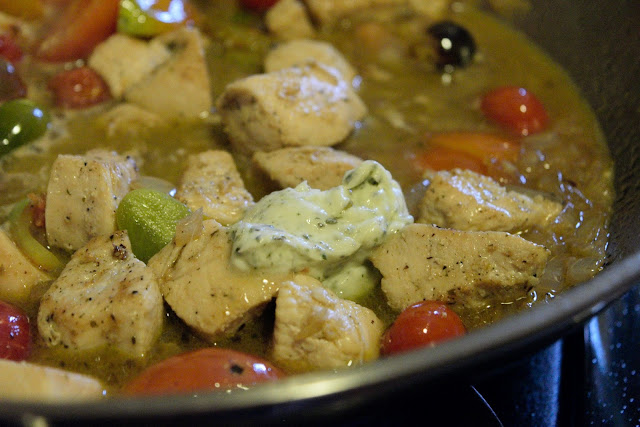 A pat of the Tuscan herb butter being added to the chicken, tomatoes, onions, and garlic.