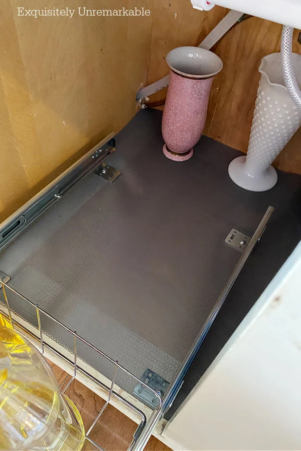 Gray shelf liner in under sink cabinet with a pink and white vase tucked inside