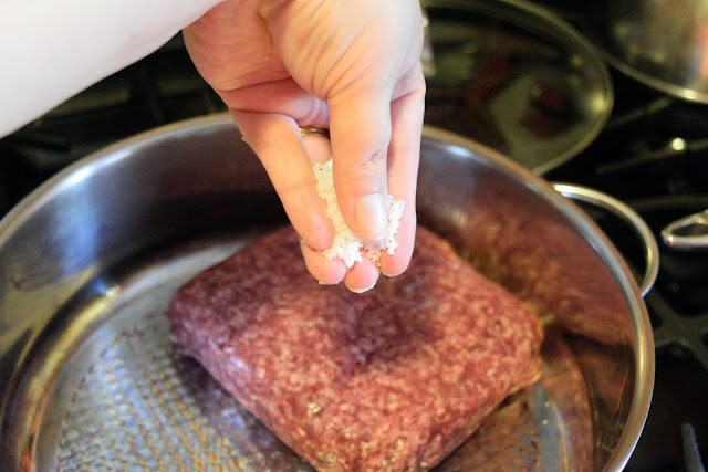 Salt being added to the ground beef on the stove.