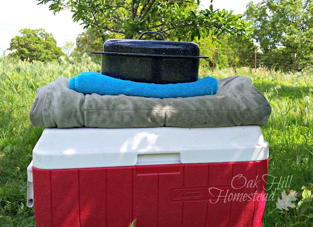 A stack of the items needed to make a straw box cooker: ice chest, blanket, bath towel and a heavy, lidded pot.