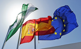 Pic of 3 flags flying at top of flagpoles in sunshine: Andalusian, Spanish and EU