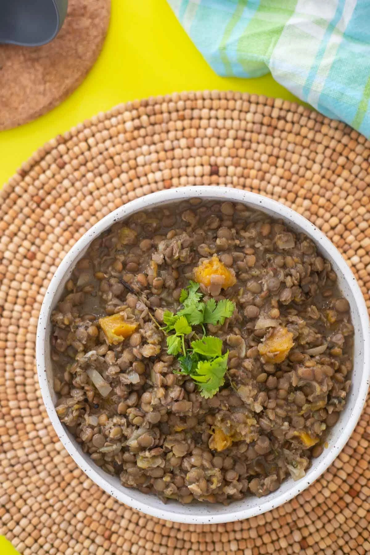 Cooked lentil peas in a white serving bowl on top of a brown placemat.