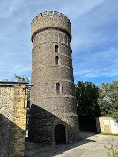 A photo of an old-fashioned looking tower with a turret (Crampton Tower). Photo by Kevin Nosferatu for the Skulferatu Project.