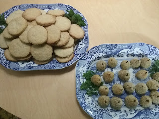 Two blue and white transferware platters, one with large gingerbread cookies, the other with small pear-shaped meatballs; both plates garnished with mint and marjoram leaves.