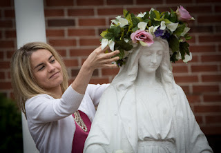 A woman crowning a statue of Mother Mary with a crown of flowers