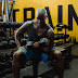 Man in blue tank top and shorts sitting on bench lifting a dumbbell