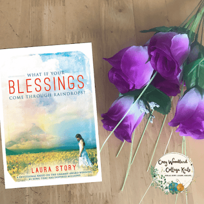 a wooden table with the book Blessings by Laura Story next to a bunch of purple roses