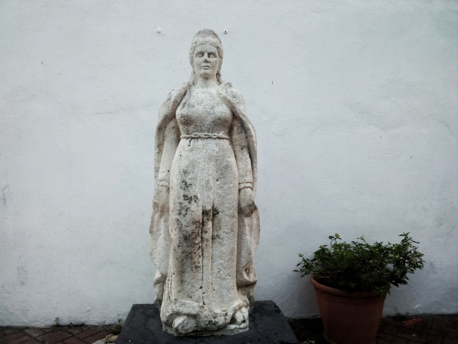 Statue of María de Toledo Statue of María de Toledo; a short, white statue of a woman wearing a 16th century dress and a cape.