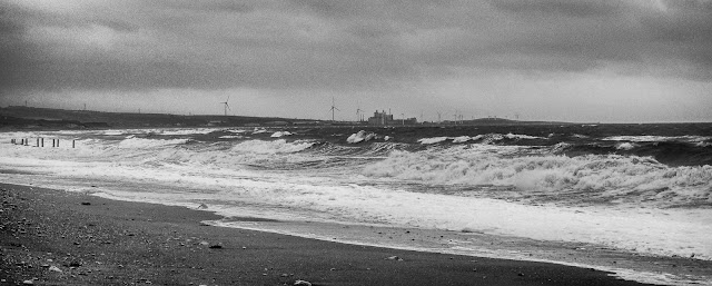 Photo of massive waves breaking on the shore with Iggesund Paperboard's Workington Mill in the distance 