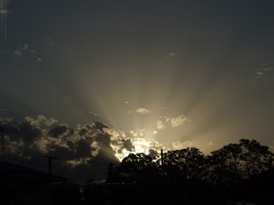 sunset with sun rays shining over urban rooftops with clouds - landscape photo of the sun setting