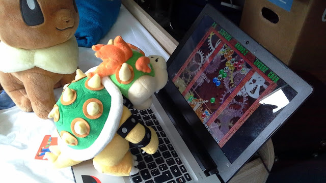 Peluche de Bowser jugando Puzzle Bobble mientras Peluche de Eevee lo mira.