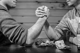 2 men arm wrestling over a pile of money