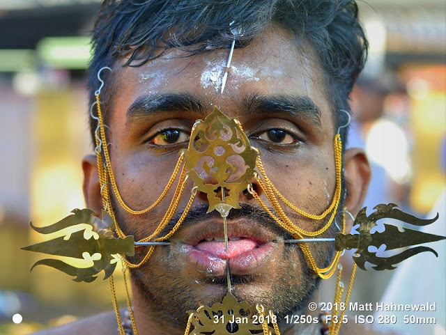 matt hahnewald photography; facing the world; hooks; skin; character; head; face; forehead; piercing; skewer; worshiper; pin; brass; eyes; lips; mouth; tongue piercing; tongue; facial expression; jewelry; consent; emotion; rapport; travel; religion; traditional; cultural; hinduism; festival; celebration; devotee; thaipusam; penang; georgetown; malaysia; asia; tamil; malaysian indian; asian; one person; male; young; man; image; photo; illustrative editorial; face perception; nikon d3100; nikkor af-s 50mm f/1.8g; prime lens; 50mm; nifty fifty; 4x3; horizontal; street; portrait; closeup; head shot; full-face view; outdoor; color; authentic; shutterstock; chains; pierced; devotion; pain; ethnic; needle; faith; vibhuti; sacred ash