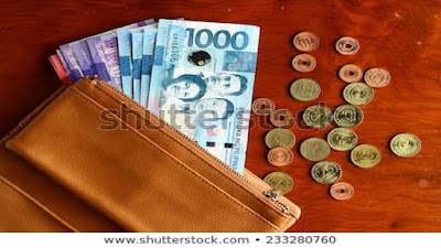 Brown wallet holding currency notes and coins on top of a brown table.