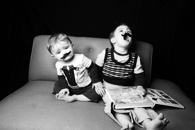 Two little boys enjoying reading books and wearing mustaches.