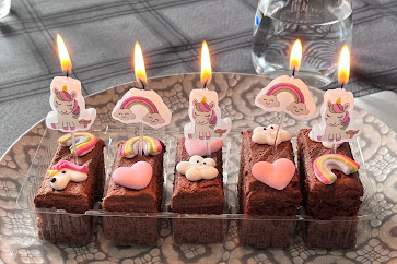 A plate with some rectangular slices of chocolate cake with decorations on top and some lit candles