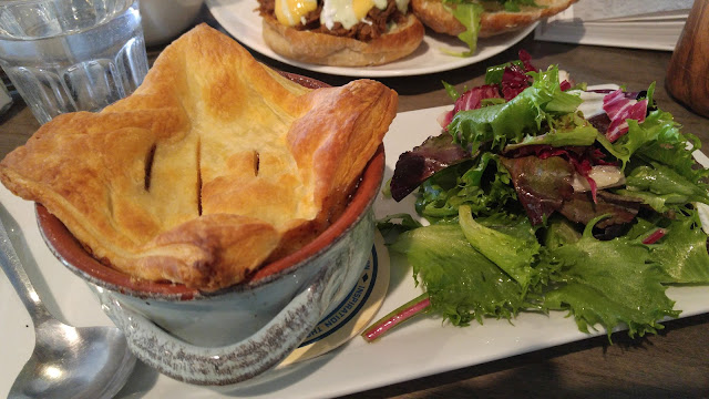 A plate containing a bowl savoury guinness steak and mushroom topped with a flaky pie crust beside a small salad of mixed greens. 