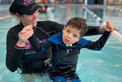 Image of a swimming instructor in the pool holding her student out of the water. Traumatic Brain Injury: Aquatic Therapy