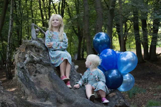 Sitting on an uprooted tree with a bunch of balloons not looking at the camera