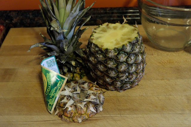 A whole pineapple, on a cutting board, with the top and bottom cut off.