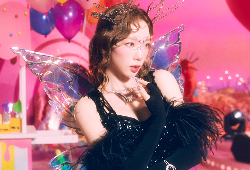 Taeyeon dressed in a black outfit like a fairy, with her hair tightly curled to her face, and fairy wings. This shot is from the ‘Cosmic Fiesta’ concept for Forever 1.