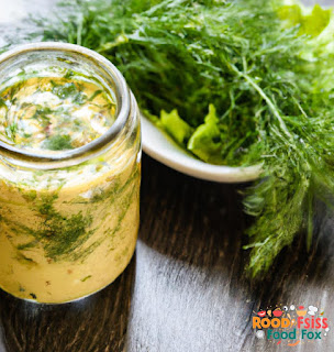 A jar of creamy lemon dill dressing with a sprig of fresh dill on top.