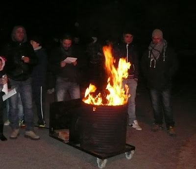 Bidón en el que arde una hoguera. Detrás cinco marzantes.