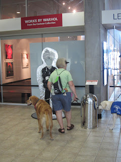 Here Denny and puppy raiser Sylvia approach a life size cut out of Andy Warhol.