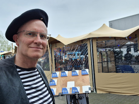 Karikaturist Hugo met alpino, streepjesshirt, gilet en tekenstatief met bierviltjes op foodtruck festival outdoor event