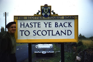 Charles standing in front of Haste Ye Back to Scotland sign